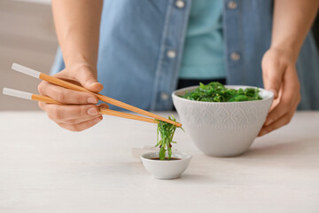 Woman eating tasty seaweed salad in kitchen