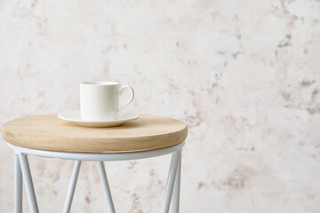 Stylish table with cup near light wall in room