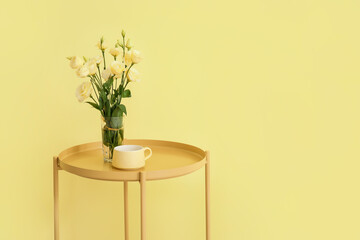 Stylish table with flowers and cup near color wall in room
