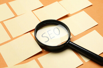 Paper sheets with abbreviation SEO and magnifier on color background