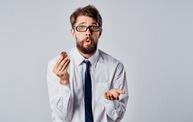 A man with a gold coin in his hands on a light background puzzled look of the Bitcoin cryptocurrency business