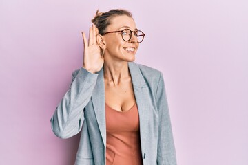 Beautiful caucasian woman wearing business jacket and glasses smiling with hand over ear listening an hearing to rumor or gossip. deafness concept.