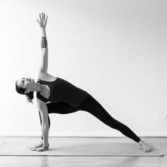 A dark-haired European woman in her 30’s practices yoga at home. Meditation, stretching and mindfulness to achieve physical and spiritual health. Black and white square format