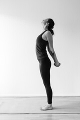 Dark-haired 30's European woman stretches arms behind back opening shoulders during yoga at home. Meditation and mindfulness to achieve physical and spiritual health. Black and white vertical format