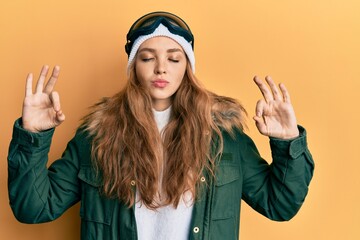 Beautiful blonde caucasian woman wearing snow wear and sky glasses relax and smiling with eyes closed doing meditation gesture with fingers. yoga concept.