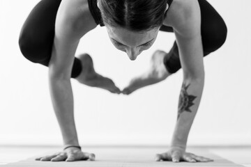 A brunette woman in her 30’s practicing yoga at home. One woman concentrated on a balance arm-pressing asana, or yoga posture. Black and white horizontal image