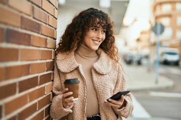 Young hispanic woman smiling happy using smartphone and drinking coffee at the city