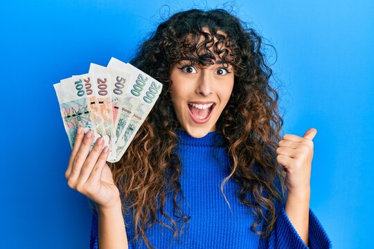 Young hispanic girl holding czech koruna banknotes pointing thumb up to the side smiling happy with open mouth