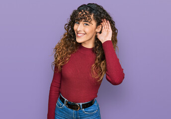 Young hispanic girl wearing casual clothes smiling with hand over ear listening an hearing to rumor or gossip. deafness concept.