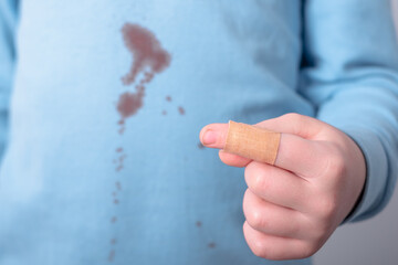 Closeup of kid finger with sticking-plaster. dirty blood stain on t-shirt on the background. place for text