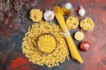 Above view of uncooked pastas in various forms as spaggeti garlic and onion oil bottle on mixed color background