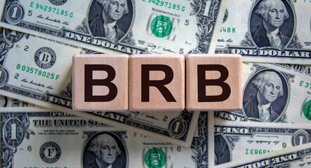 BRB symbol. Wooden cubes with word 'BRB - be right back' on a beautiful background from dollar bills. Business and BRB concept, copy space.