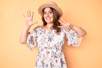 Young beautiful caucasian woman wearing summer dress and hat showing and pointing up with fingers number nine while smiling confident and happy.