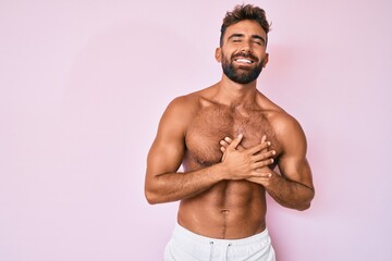 Young hispanic man standing shirtless smiling with hands on chest with closed eyes and grateful gesture on face. health concept. - Powered by Adobe