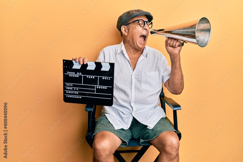 Sticker Handsome mature director man holding video film clapboard and louder angry and mad screaming frustrated and furious, shouting with anger. rage and aggressive concept.