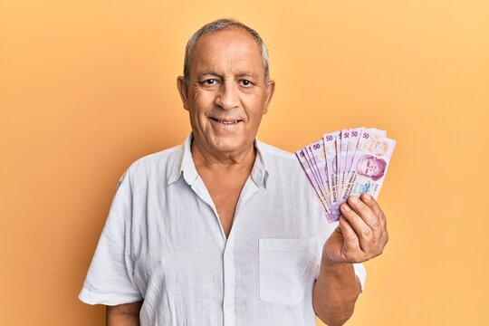 Handsome mature man holding 50 mexican pesos banknotes looking positive and happy standing and smiling with a confident smile showing teeth