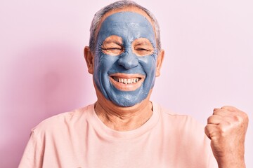 Senior man with grey hair wearing mud mask celebrating surprised and amazed for success with arms raised and eyes closed