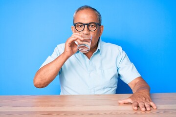 Handsome senior man sitting on the table at home drinking a glass of fresh water