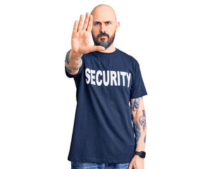 Young handsome man wearing security t shirt doing stop sing with palm of the hand. warning...