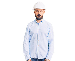 Young handsome man wearing architect hardhat relaxed with serious expression on face. simple and natural looking at the camera.