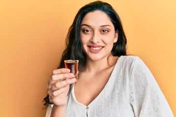 Beautiful middle eastern woman drinking whiskey shot looking positive and happy standing and smiling with a confident smile showing teeth - Powered by Adobe