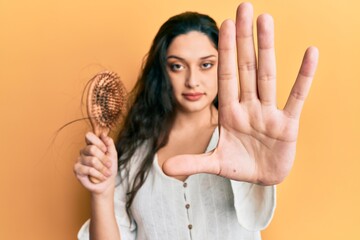 Beautiful middle eastern woman holding comb loosing hair with open hand doing stop sign with serious and confident expression, defense gesture