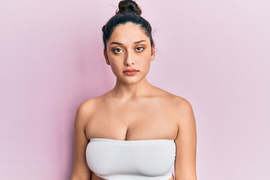 Beautiful middle eastern woman standing wearing a top showing skin with serious expression on face. simple and natural looking at the camera.