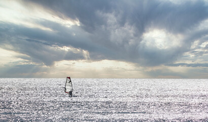 Windsurfer furrowing a silver sea by the reflections of the sun on a cloudy day