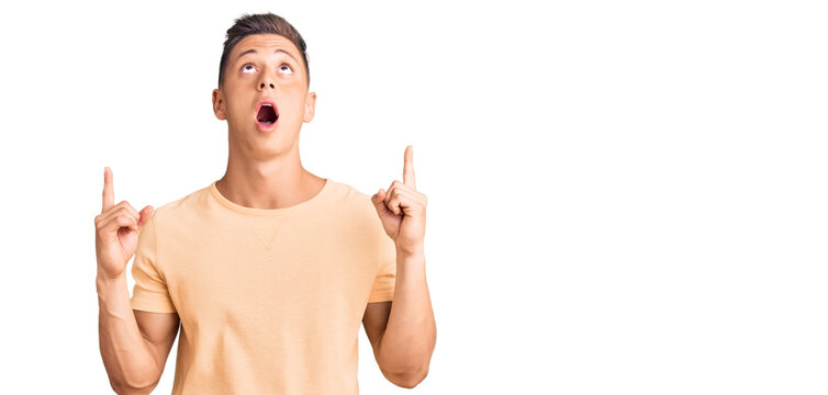 Young handsome man wearing casual clothes amazed and surprised looking up and pointing with fingers and raised arms.