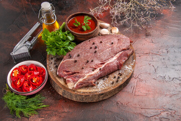 Side view of red meat on wooden tray and garlic green ketchup and chopped pepper oil bottle on dark background