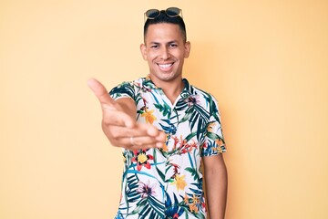 Young handsome latin man wearing summer clothes smiling friendly offering handshake as greeting and welcoming. successful business.