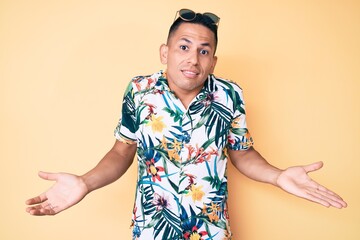 Young handsome latin man wearing summer clothes clueless and confused expression with arms and...