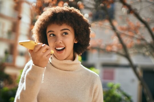 Young hispanic girl smiling happy sending voice message using smartphone at the city.