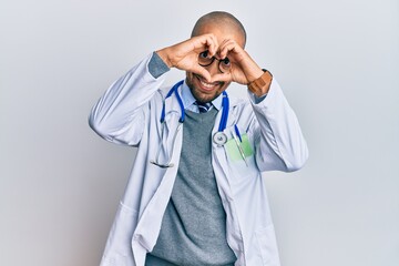 Hispanic adult man wearing doctor uniform and stethoscope doing heart shape with hand and fingers smiling looking through sign