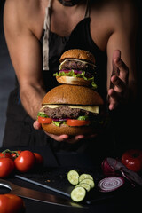 Cook in an apron on a naked body. Big and delicious Burger. Fast food.