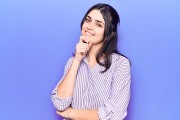 Fototapeta premium Young beautiful girl wearing casual striped shirt smiling looking confident at the camera with crossed arms and hand on chin. thinking positive.