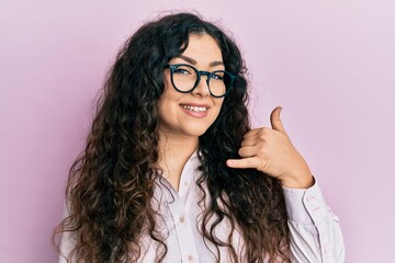 Obraz premium Young brunette woman with curly hair wearing casual clothes and glasses smiling doing phone gesture with hand and fingers like talking on the telephone. communicating concepts.