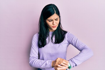 Young hispanic woman wearing casual clothes checking the time on wrist watch, relaxed and confident