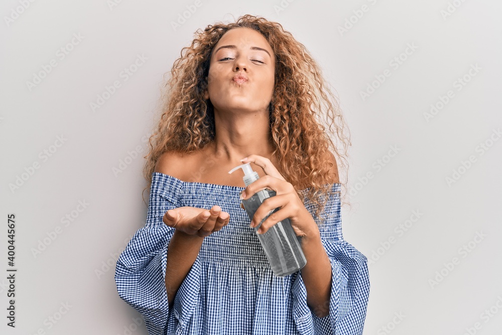 Poster beautiful caucasian teenager girl using hand sanitizer gel looking at the camera blowing a kiss bein