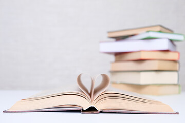 Love of books, reading, a stack of books lying on the table and open book with curled leaves in the shape of a heart in front of them, copy space