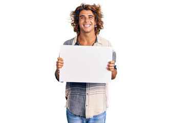 Young hispanic man holding blank empty banner looking positive and happy standing and smiling with...