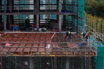 Building construction team working around scaffold, wearing safety equipment, construction helmet, safety net, gloves, protective suit, in a rainy day