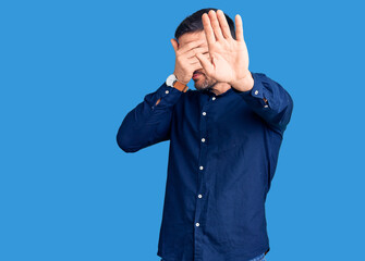 Young handsome man wearing casual shirt covering eyes with hands and doing stop gesture with sad and fear expression. embarrassed and negative concept.