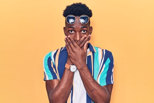 Young african american man wearing summer clothes and sunglasses shocked covering mouth with hands for mistake. secret concept.