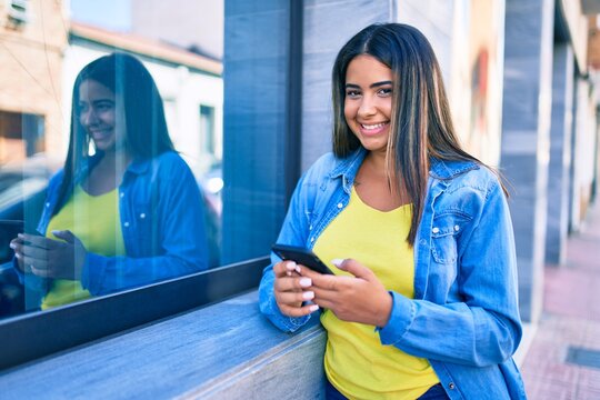 Young latin woman smiling happy using smartphone at the city.