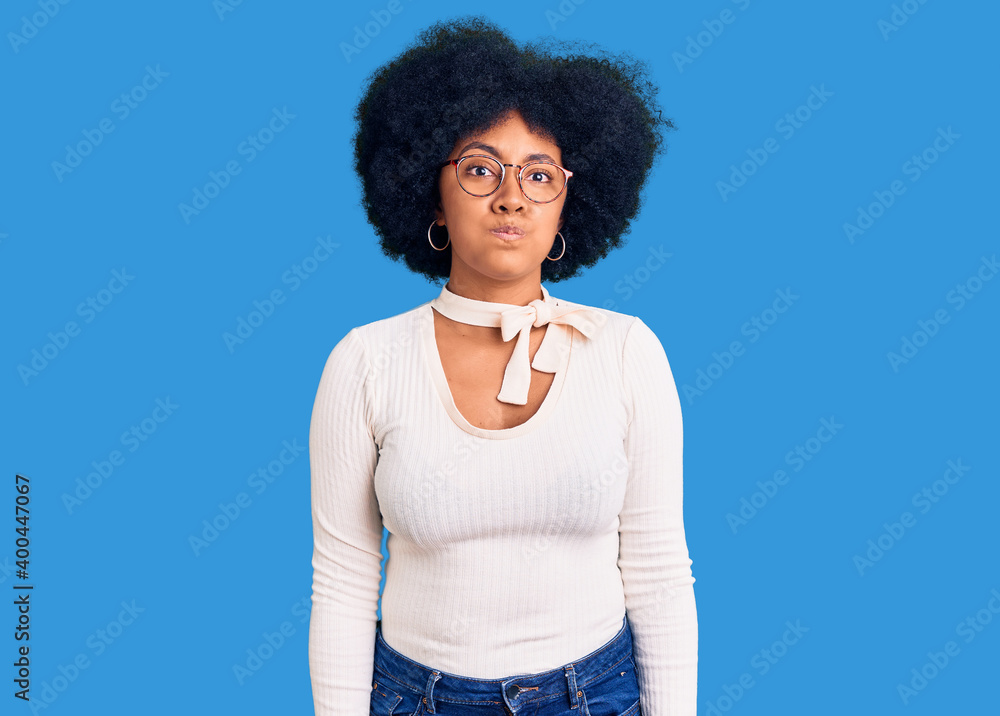 Poster Young african american girl wearing casual clothes and glasses puffing cheeks with funny face. mouth inflated with air, crazy expression.