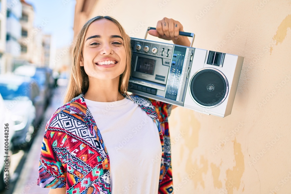 Wall mural Young beautiful blonde caucasian woman smiling happy outdoors on a sunny day playing music on boombox