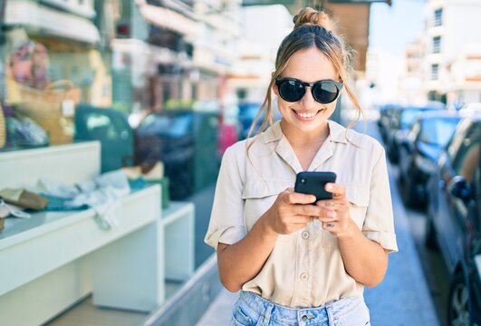 Young beautiful blonde caucasian woman smiling happy outdoors on a sunny day using smartphone