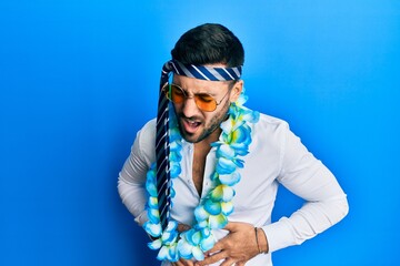 Young hispanic businessman wearing party funny style with tie on head with hand on stomach because...