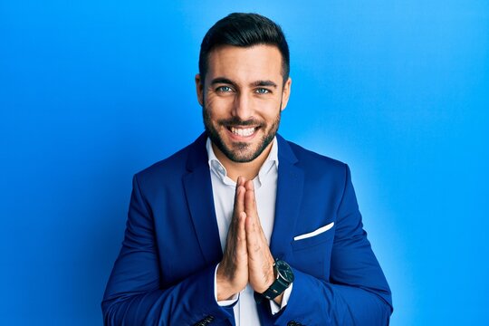 Young hispanic businessman wearing business jacket praying with hands together asking for forgiveness smiling confident.